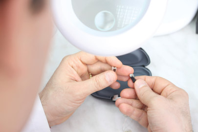 A male audiologist repairs a hearing aid by replacing broken parts, saving his patient money and improving their hearing